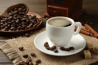 Photo of Aromatic coffee in cup, beans, brown sugar and cinnamon on wooden table, closeup