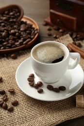 Photo of Aromatic coffee in cup, beans, brown sugar and cinnamon on table, closeup