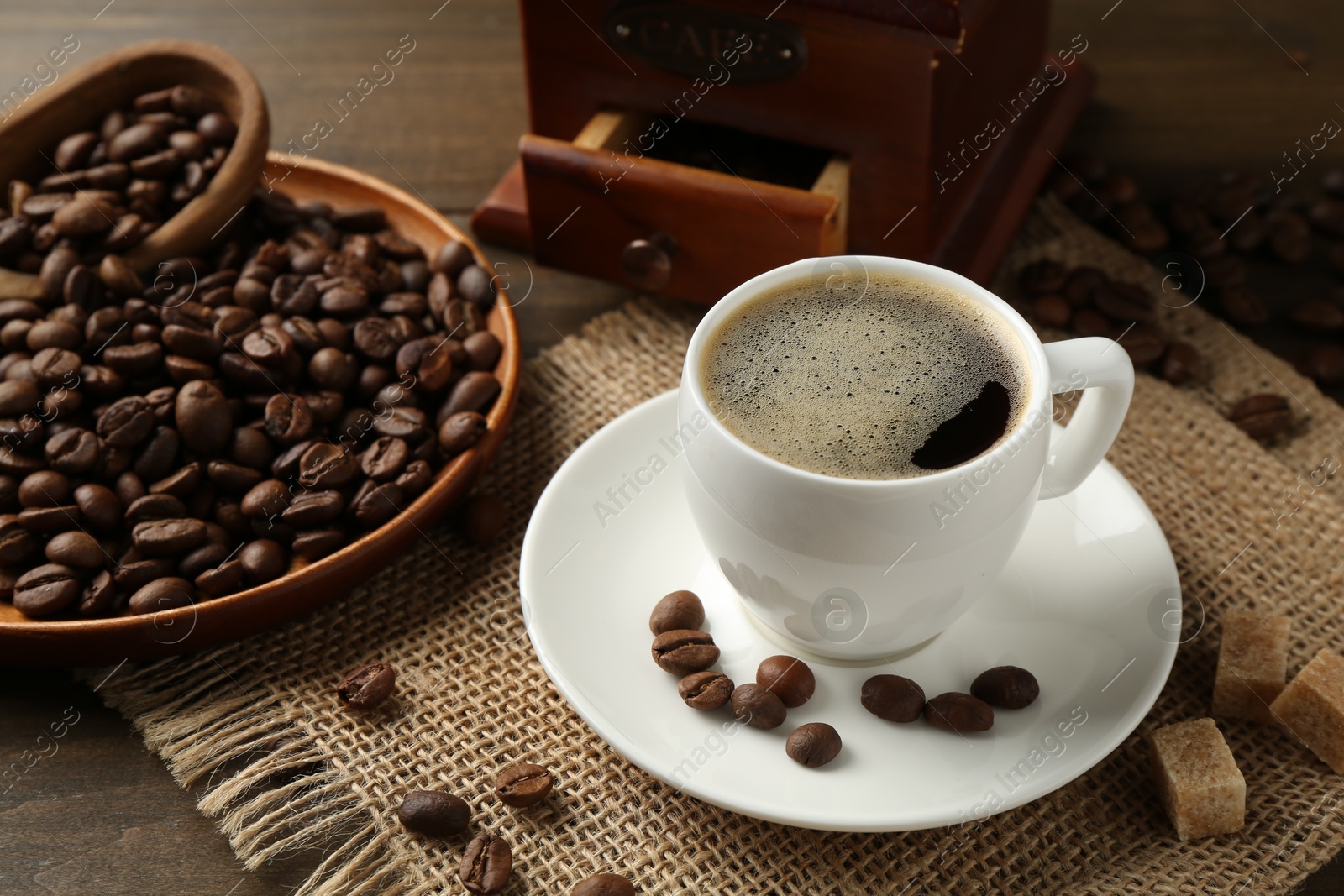 Aromatic coffee in cup, beans, brown sugar and grinder on wooden table, closeup Photo of Aromatic coffee in cup, beans, brown sugar and grinder on wooden table, closeup