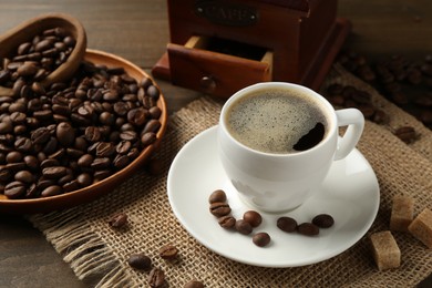 Photo of Aromatic coffee in cup, beans, brown sugar and grinder on wooden table, closeup