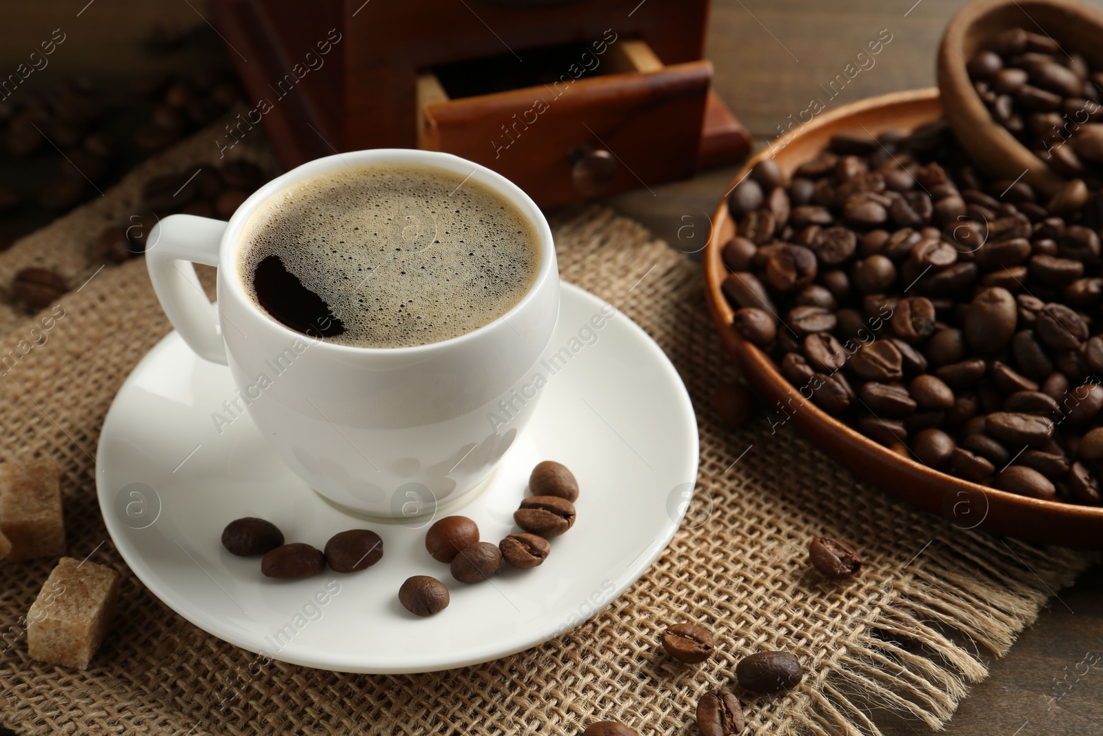 Aromatic coffee in cup, beans, brown sugar and grinder on table, closeup Photo of Aromatic coffee in cup, beans, brown sugar and grinder on table, closeup