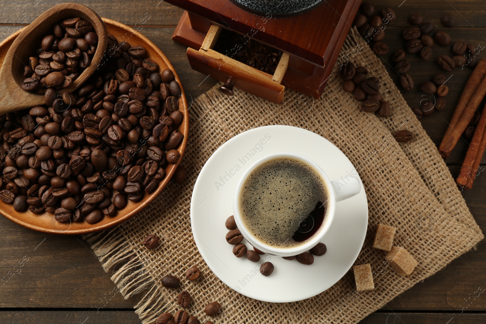 Aromatic coffee in cup, beans, brown sugar and grinder on wooden table, flat lay Photo of Aromatic coffee in cup, beans, brown sugar and grinder on wooden table, flat lay
