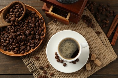 Photo of Aromatic coffee in cup, beans, brown sugar and grinder on wooden table, flat lay