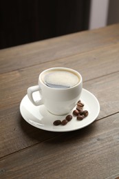 Photo of Aromatic coffee in cup and beans on wooden table