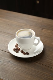 Photo of Aromatic coffee in cup and beans on wooden table