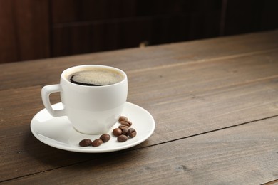 Photo of Aromatic coffee in cup and beans on wooden table, closeup. Space for text
