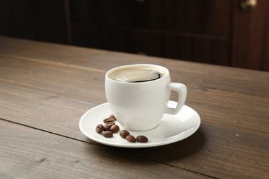 Photo of Aromatic coffee in cup and beans on wooden table, closeup