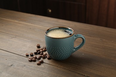 Photo of Aromatic coffee in cup and beans on wooden table