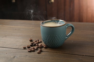 Photo of Aromatic coffee in cup and beans on wooden table