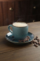 Photo of Aromatic coffee in cup and beans on wooden table, closeup