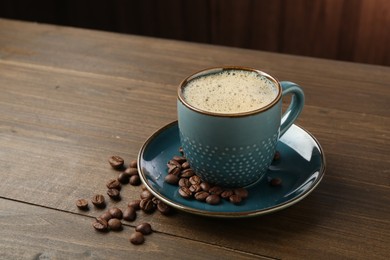 Photo of Aromatic coffee in cup and beans on wooden table, closeup. Space for text