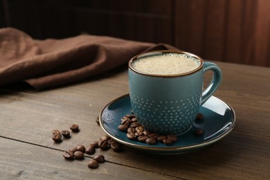 Photo of Aromatic coffee in cup and beans on wooden table, closeup. Space for text
