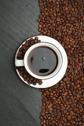 Photo of Aromatic coffee in cup and beans on black table, flat lay