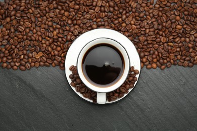 Photo of Aromatic coffee in cup and beans on black table, flat lay