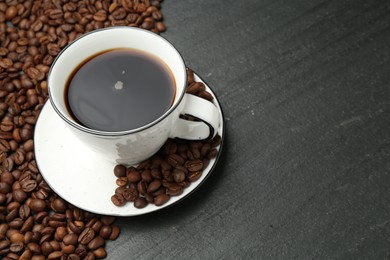 Photo of Aromatic coffee in cup and beans on black table, above view. Space for text