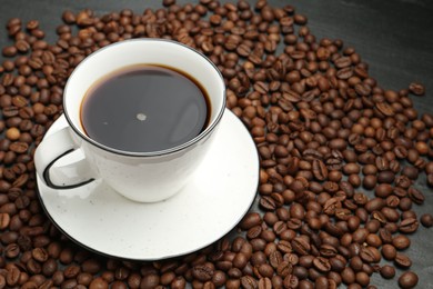 Photo of Aromatic coffee in cup and beans on black table, closeup. Space for text