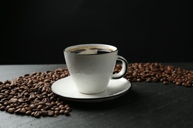 Photo of Aromatic coffee in cup and beans on black table, closeup