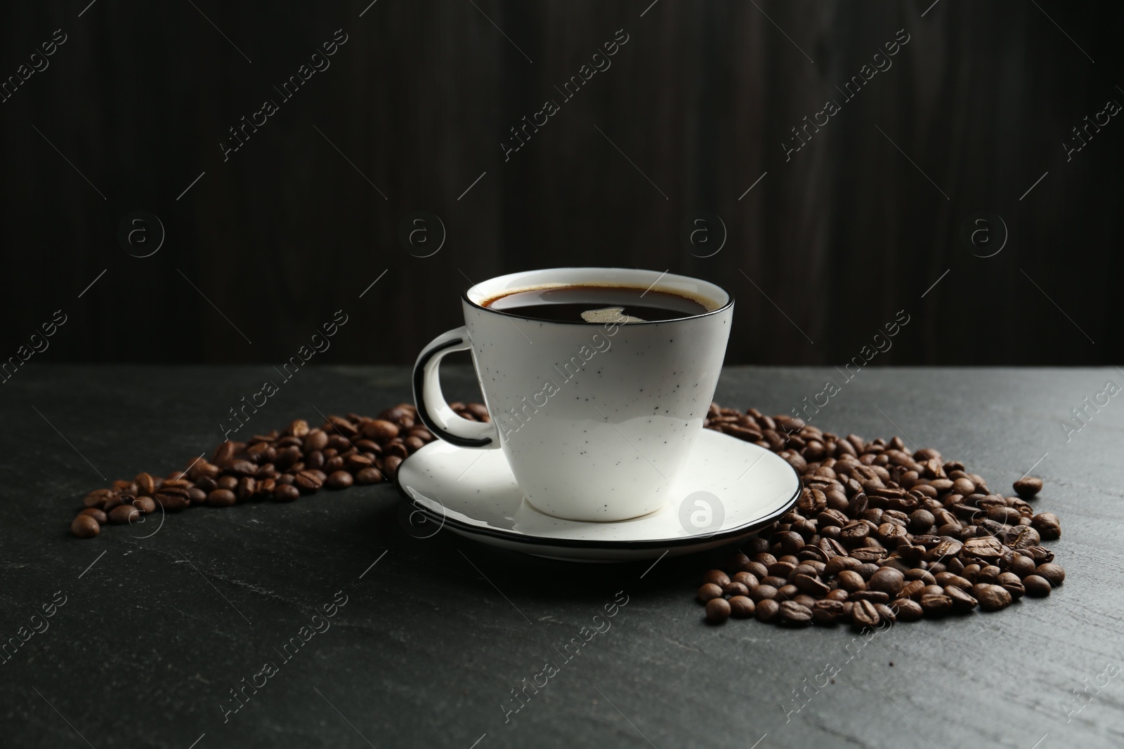 Aromatic coffee in cup and beans on black table Photo of Aromatic coffee in cup and beans on black table