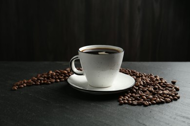Photo of Aromatic coffee in cup and beans on black table