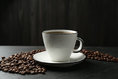 Photo of Aromatic coffee in cup and beans on black table, closeup