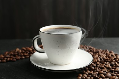 Photo of Aromatic coffee in cup and beans on black table, closeup
