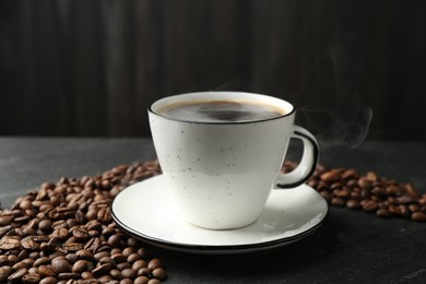 Photo of Aromatic coffee in cup and beans on black table, closeup