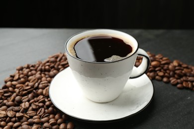 Photo of Aromatic coffee in cup and beans on black table, closeup