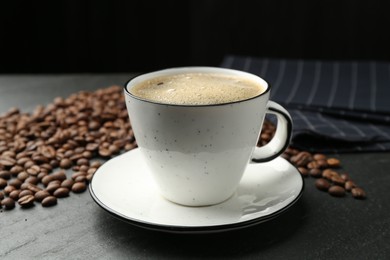Photo of Aromatic coffee in cup and beans on black table, closeup