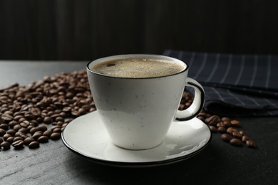 Photo of Aromatic coffee in cup and beans on black table, closeup