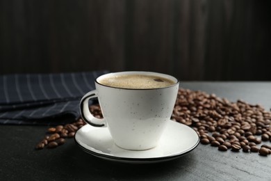 Photo of Aromatic coffee in cup and beans on black table, closeup