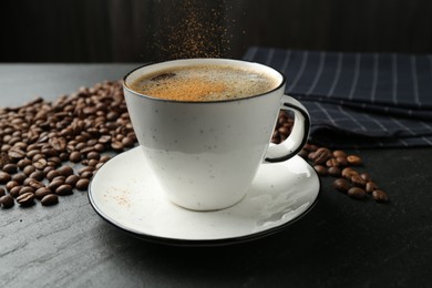 Photo of Adding cinnamon to aromatic coffee at black table, closeup