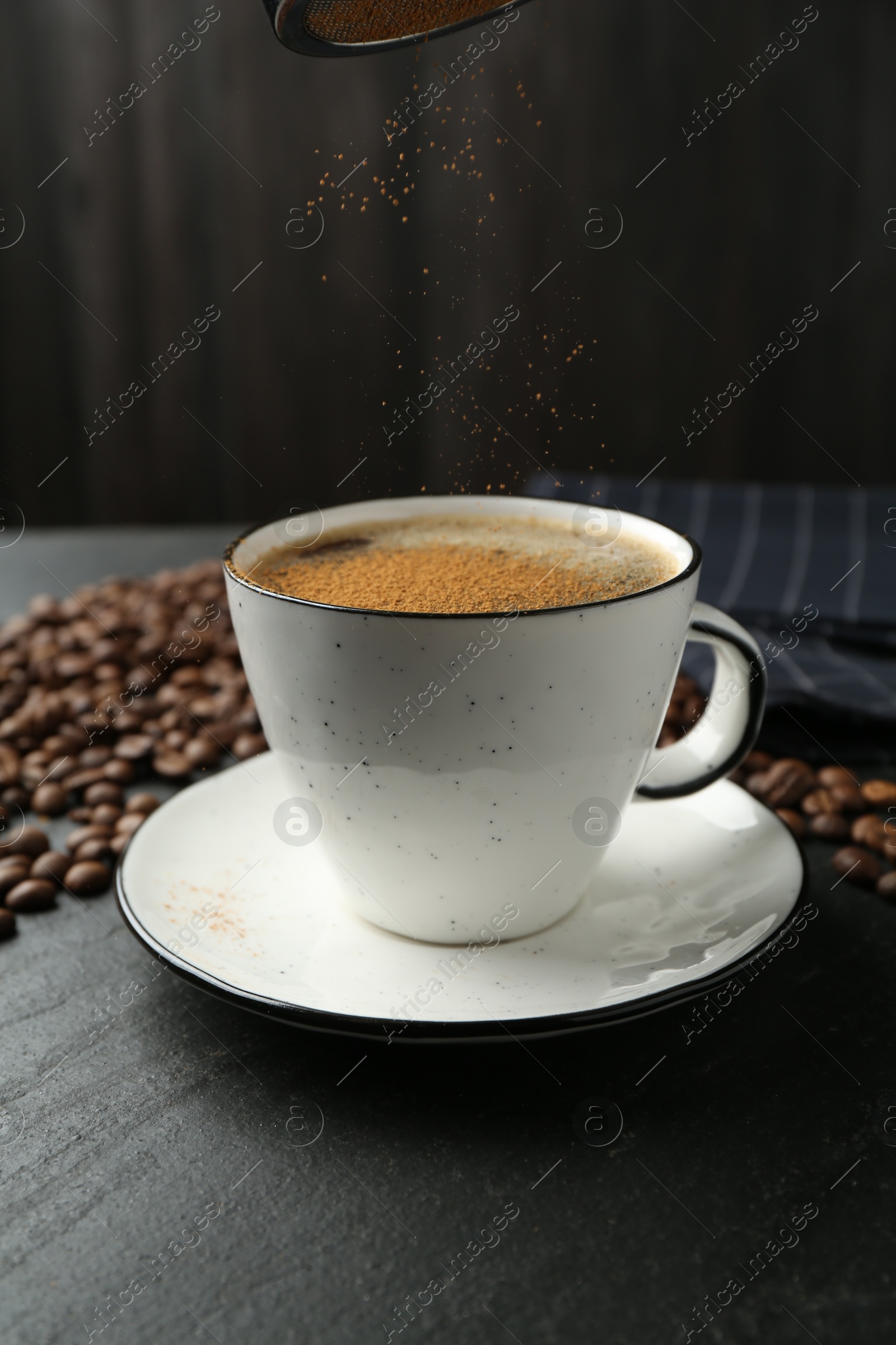 Adding cinnamon to aromatic coffee at black table, closeup Photo of Adding cinnamon to aromatic coffee at black table, closeup