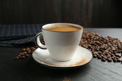 Photo of Adding cinnamon to aromatic coffee at black table, closeup