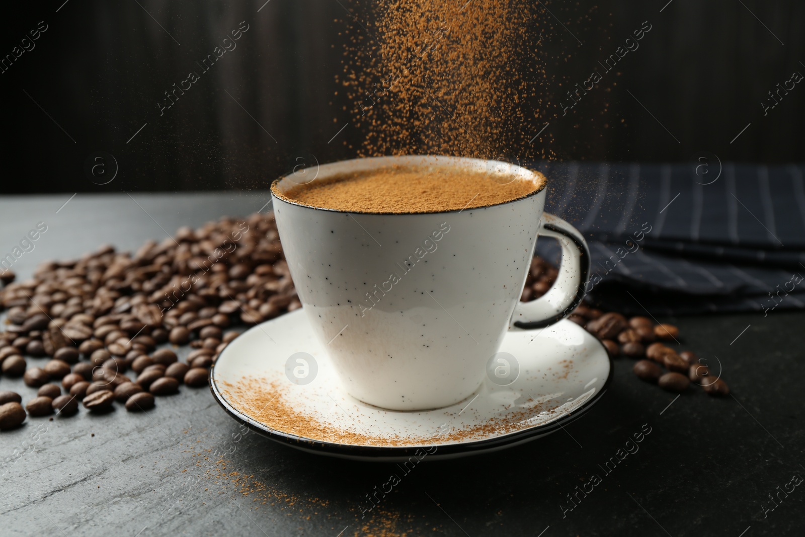 Adding cinnamon to aromatic coffee at black table, closeup Photo of Adding cinnamon to aromatic coffee at black table, closeup