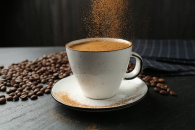 Photo of Adding cinnamon to aromatic coffee at black table, closeup