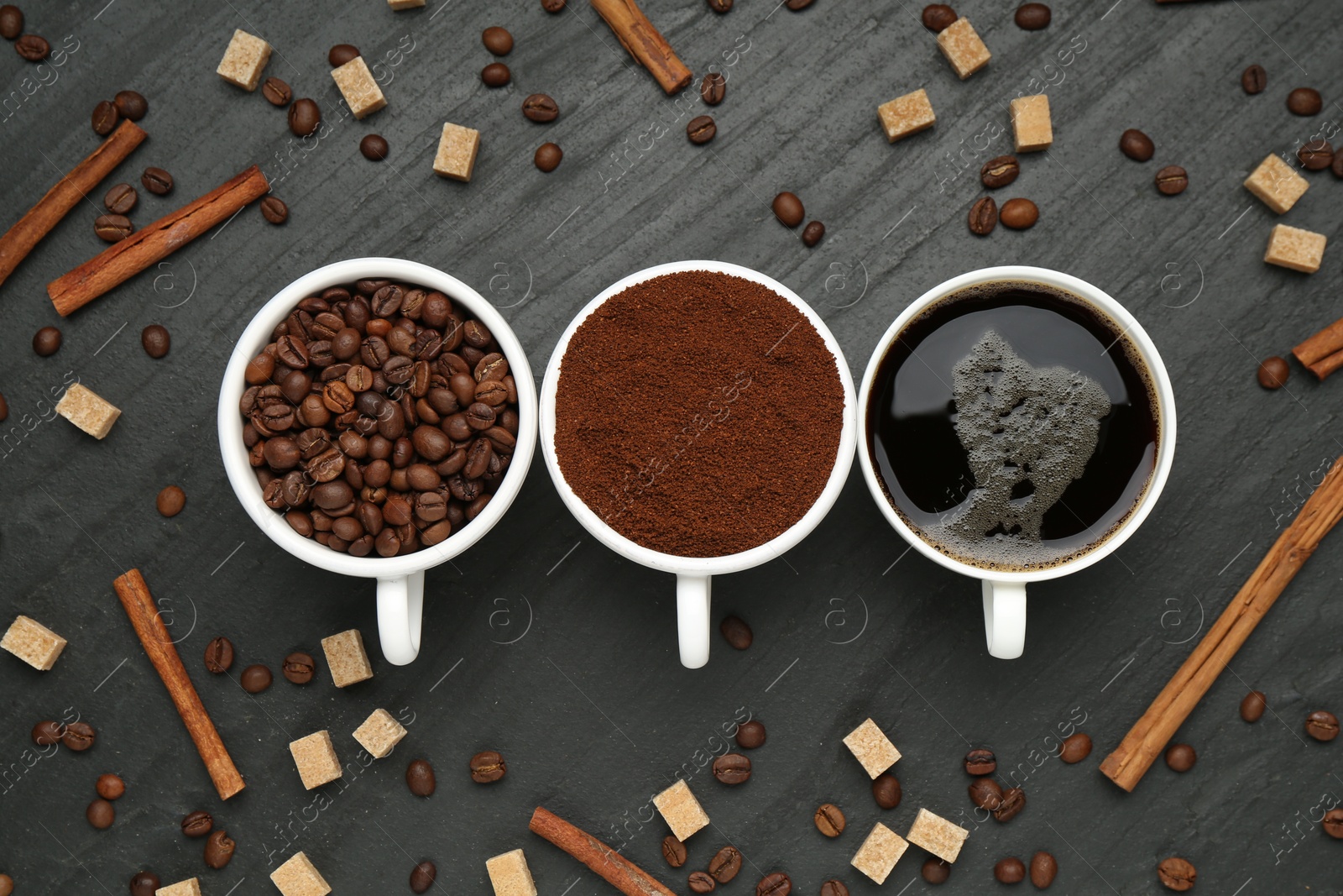 Cup of drink, ground coffee, beans, brown sugar and cinnamon on black table, flat lay Photo of Cup of drink, ground coffee, beans, brown sugar and cinnamon on black table, flat lay