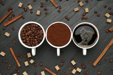 Photo of Cup of drink, ground coffee, beans, brown sugar and cinnamon on black table, flat lay