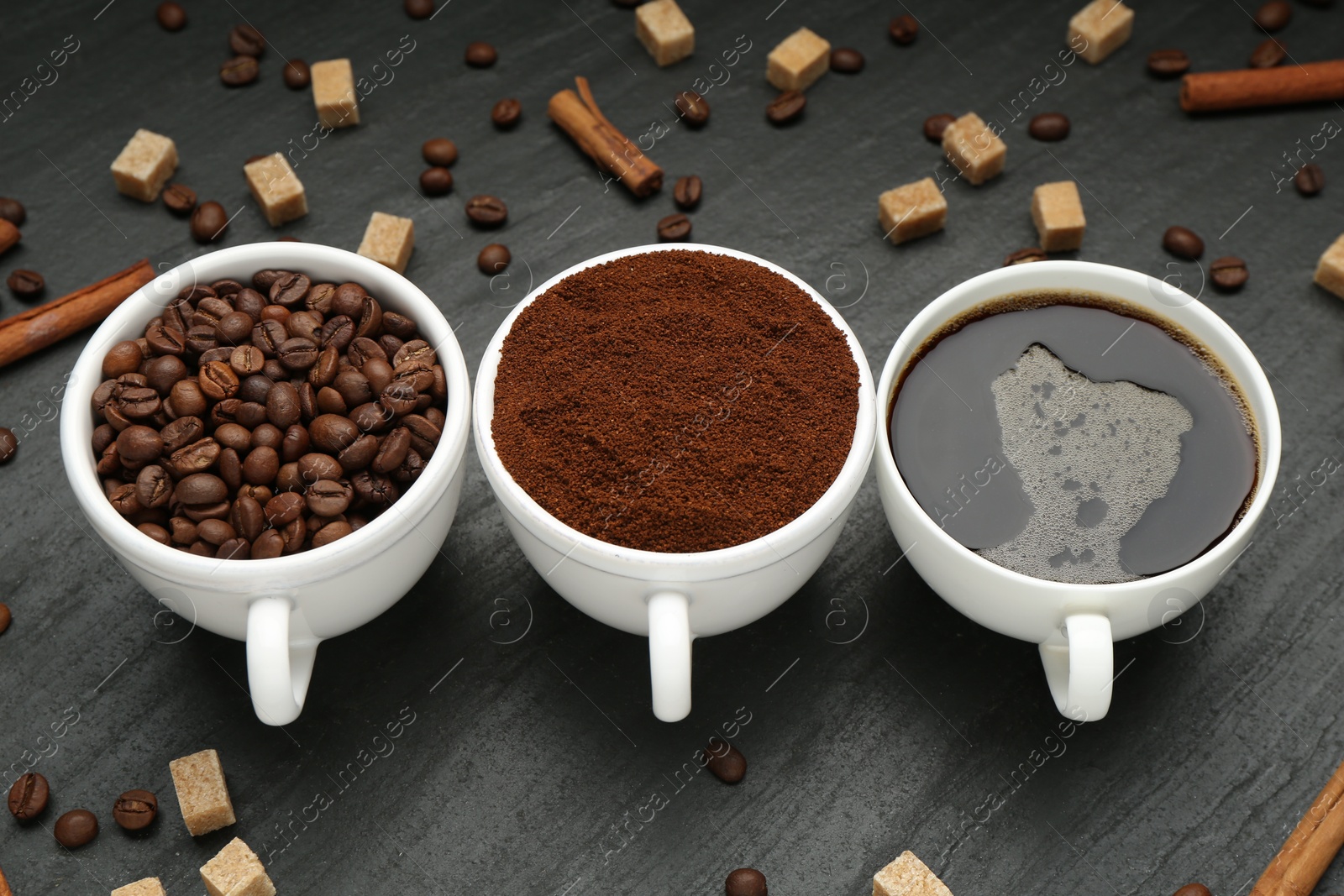 Cup of drink, ground coffee, beans, brown sugar and cinnamon on black table, above view Photo of Cup of drink, ground coffee, beans, brown sugar and cinnamon on black table, above view