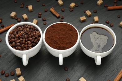 Photo of Cup of drink, ground coffee, beans, brown sugar and cinnamon on black table, above view