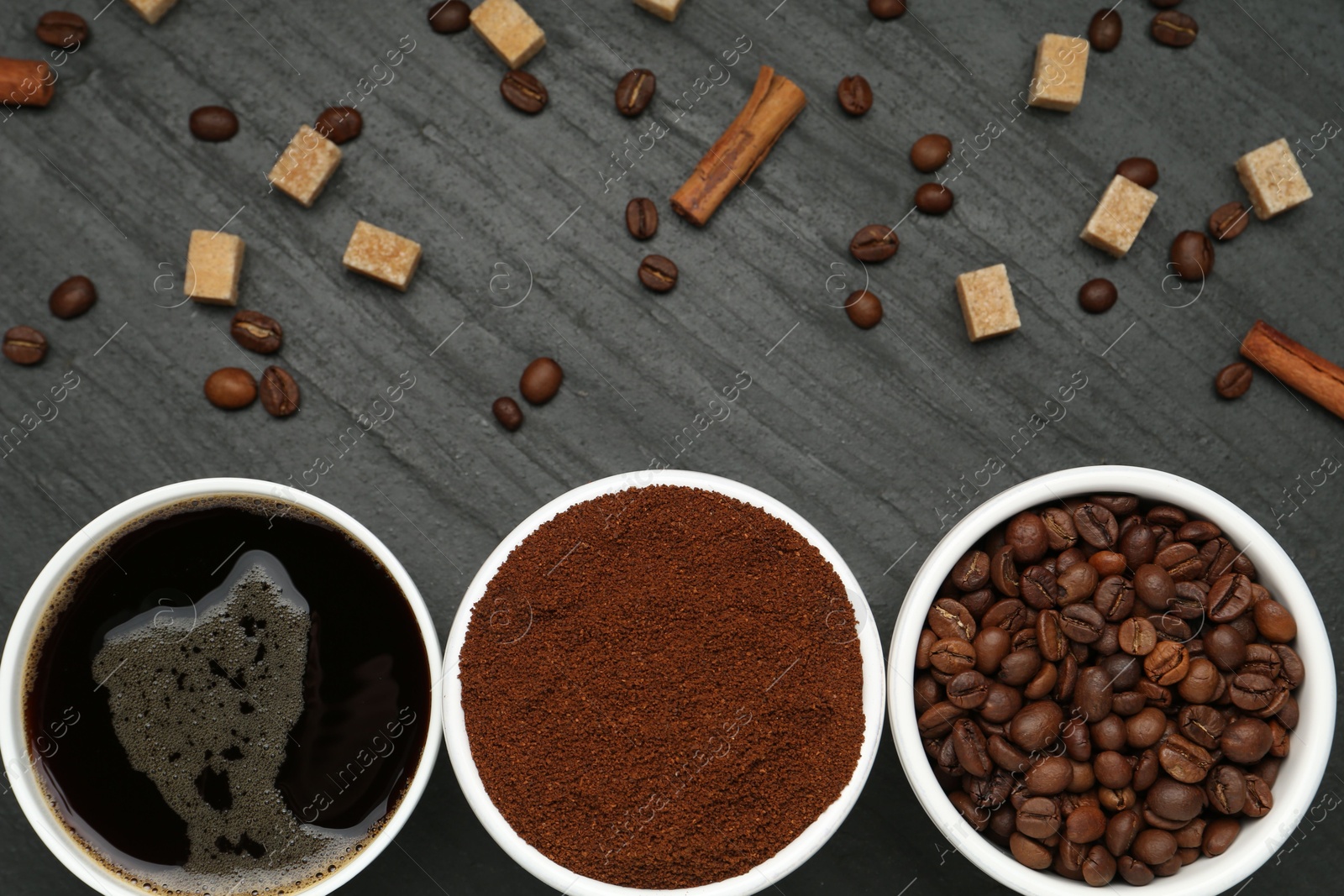 Cup of drink, ground coffee, beans, brown sugar and cinnamon on black table, flat lay Photo of Cup of drink, ground coffee, beans, brown sugar and cinnamon on black table, flat lay