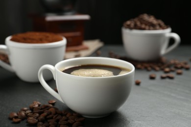 Photo of Cup of drink, ground coffee and beans on black table, closeup