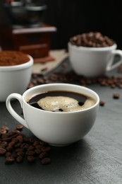 Photo of Cup of drink, ground coffee and beans on black table, closeup