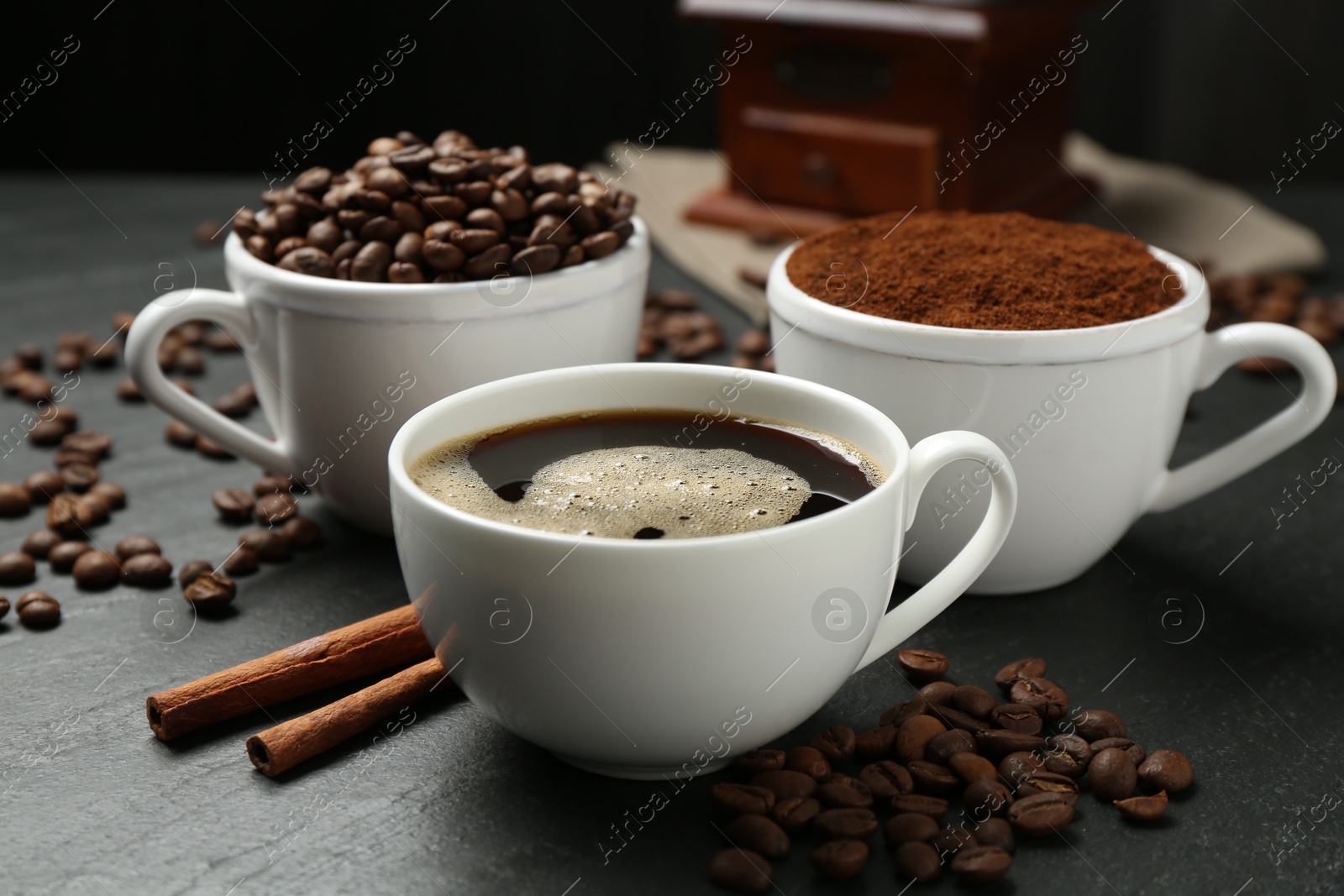 Cup of drink, ground coffee, beans and cinnamon on black table, closeup Photo of Cup of drink, ground coffee, beans and cinnamon on black table, closeup