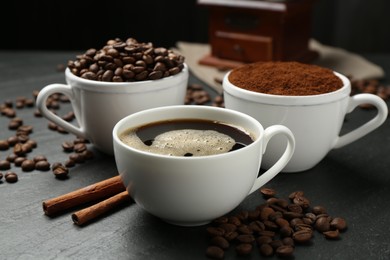 Photo of Cup of drink, ground coffee, beans and cinnamon on black table, closeup