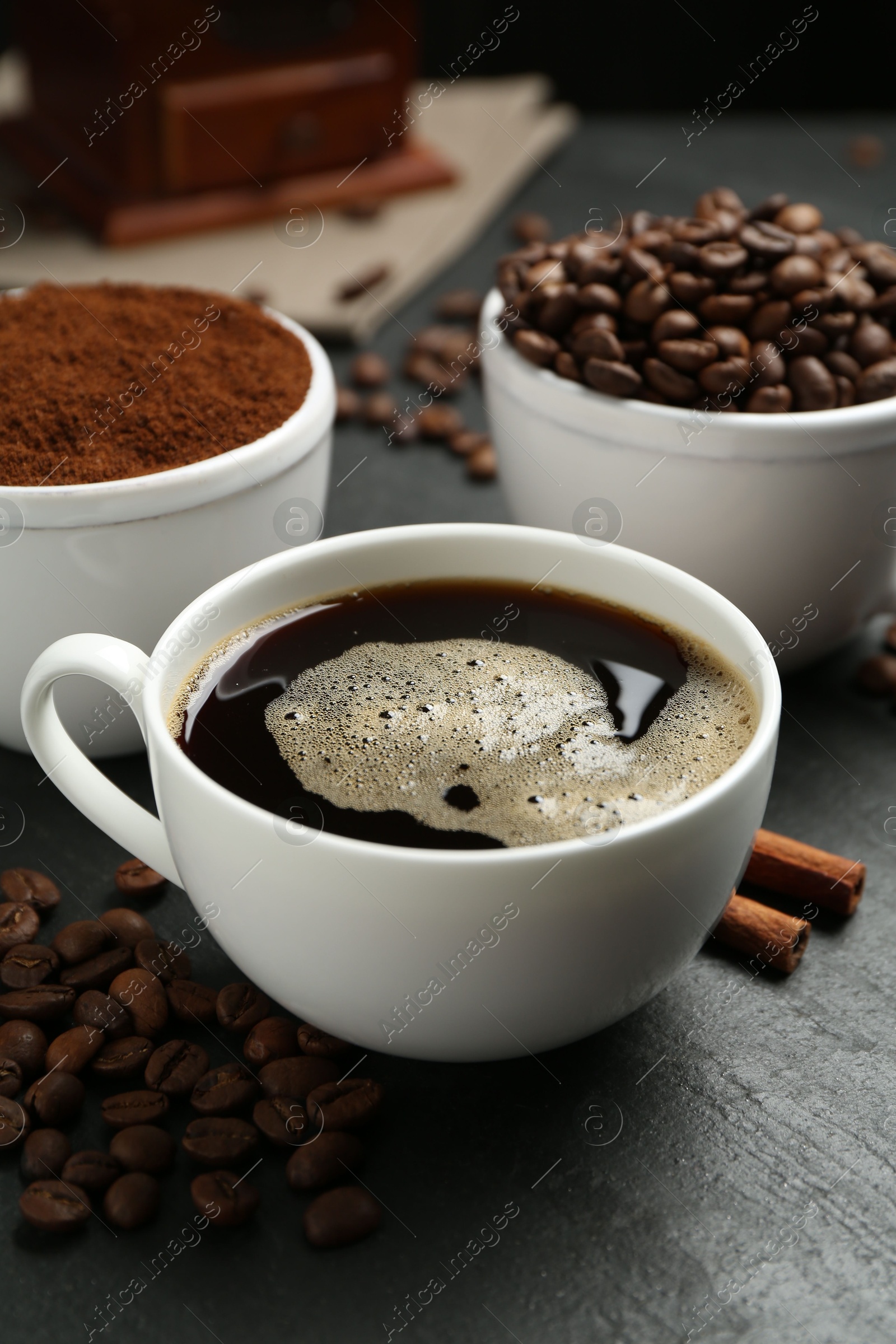 Cup of drink, ground coffee, beans and cinnamon on black table, closeup Photo of Cup of drink, ground coffee, beans and cinnamon on black table, closeup