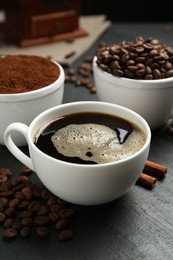 Photo of Cup of drink, ground coffee, beans and cinnamon on black table, closeup