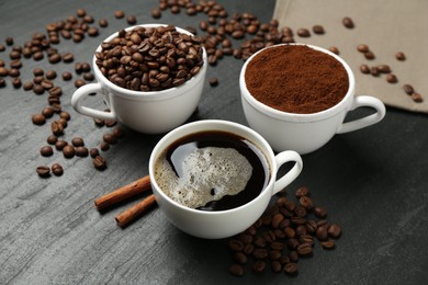 Photo of Cup of drink, ground coffee, beans and cinnamon on black table, above view