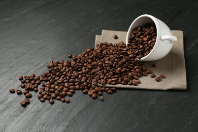 Photo of Aromatic coffee beans and overturned cup on black table