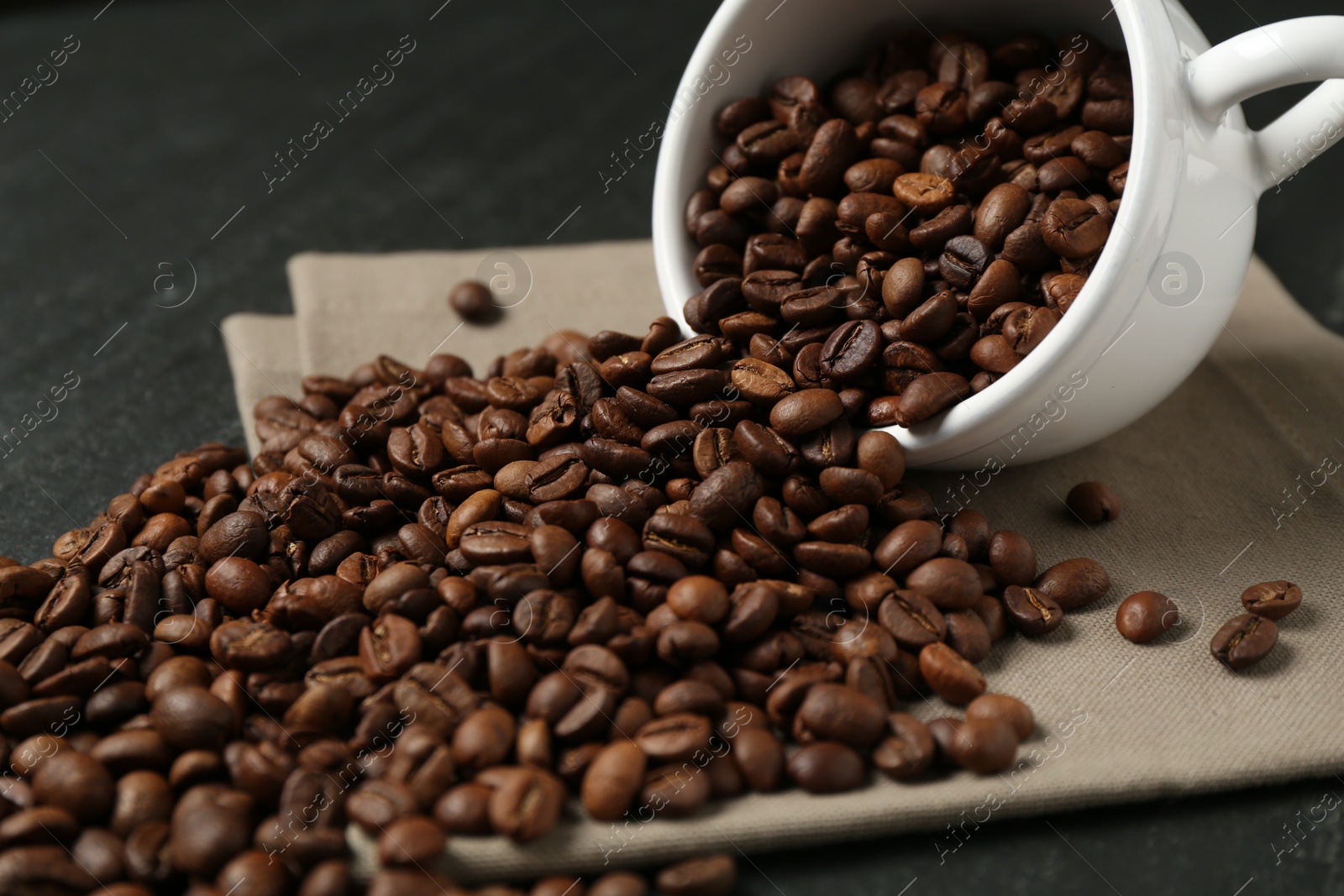 Aromatic coffee beans and overturned cup on black table, closeup Photo of Aromatic coffee beans and overturned cup on black table, closeup