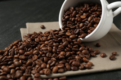Photo of Aromatic coffee beans and overturned cup on black table, closeup